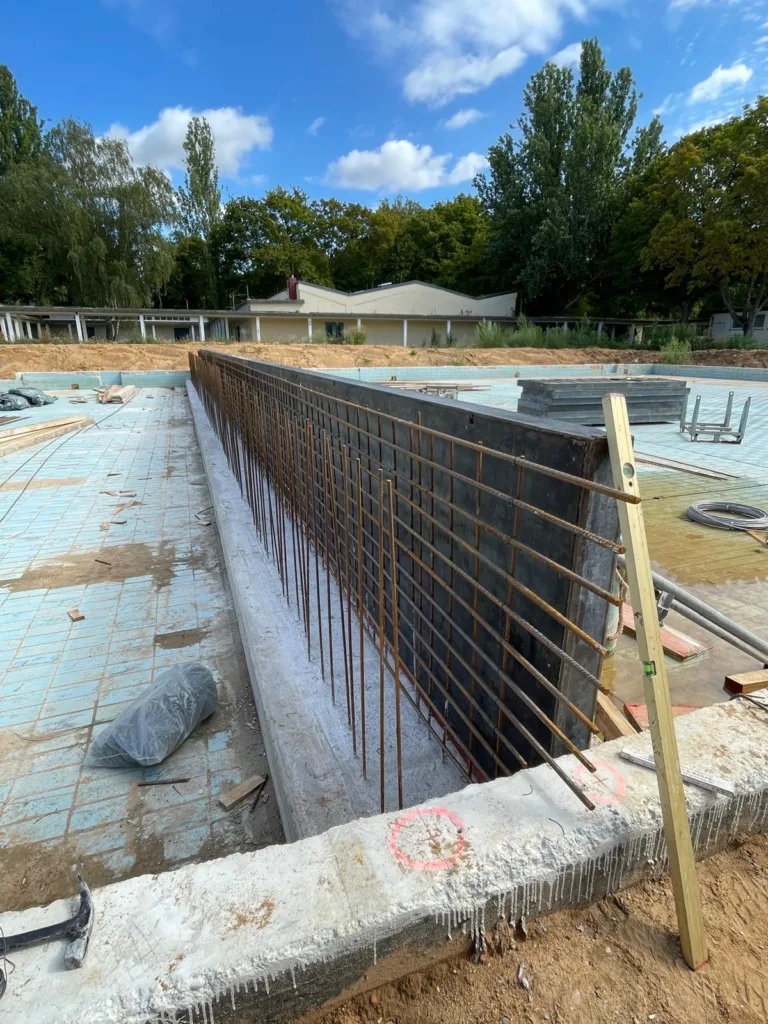 Bewehrung der neuen Beckenwand im Nichtschwimmerbecken. Ein dichtes Gitter aus Stahlstäben verläuft entlang der Schalung und wird für die spätere Betonage vorbereitet.