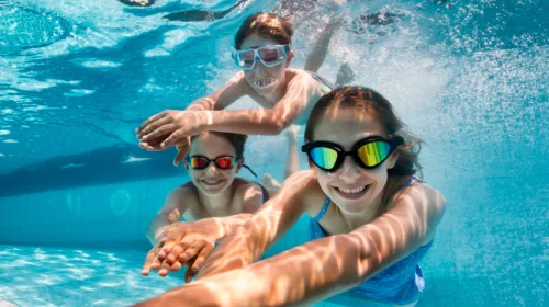 3 Kinder tauchen mit Schwimmbrillen im Schwimmbecken Unterwasser