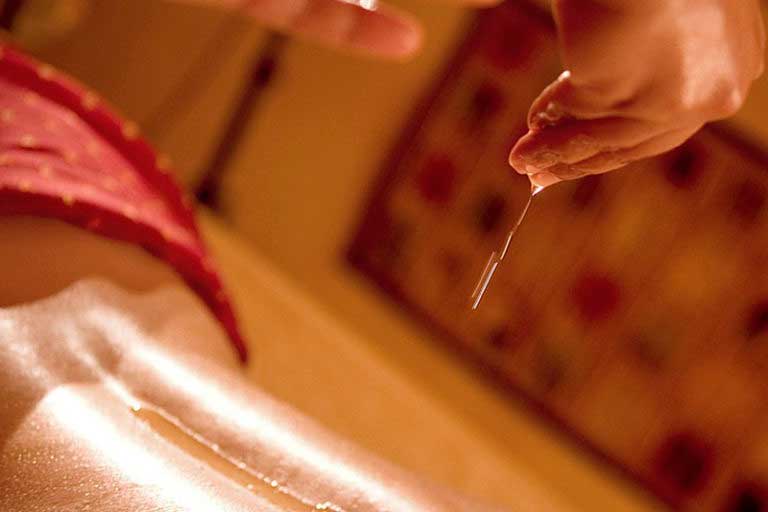 Öl wird auf einem Rücken geträufelt.